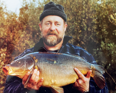 Originalfoto: Angler mit Mütze hält einen großen Karpfen vor herbstlichen Büschen